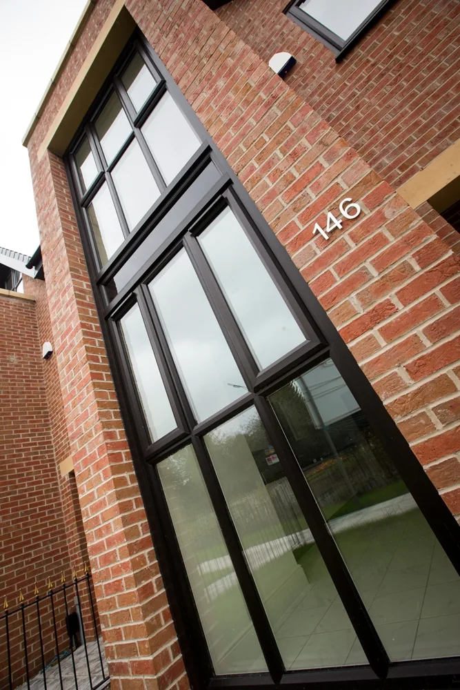 Full-height glazing reflecting the sky beside brickwork at Barton Road